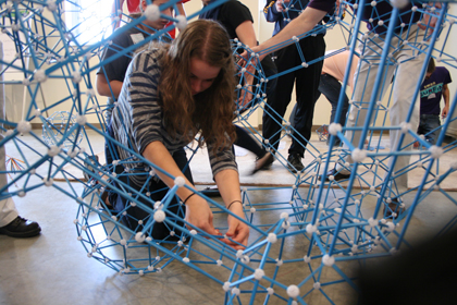 A student crouches in the middle of the structure so she can repair disconnected struts.
