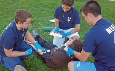 Three Medical Emergency Response Team members assist a fallen student in a training drill
