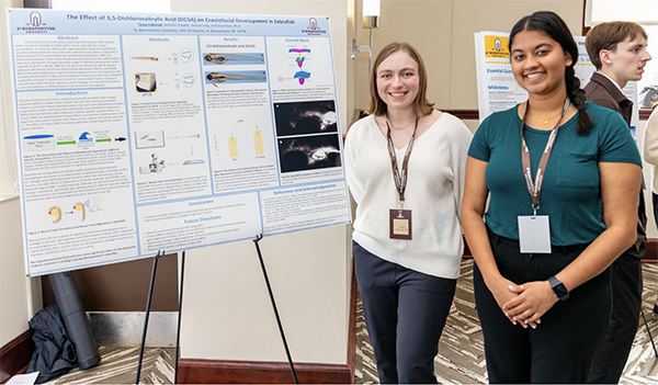 Tessa and Nishtha pose next to a poster about their research with Dr. Ryan