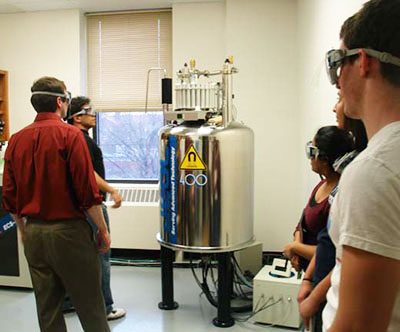 Students and a professor stand near the NMR.