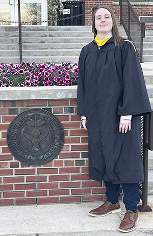 Kaitlin poses in her graduation robe in front of Plassmann