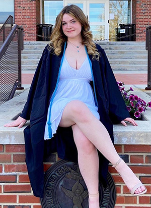Kyra poses in her graduation robe in front of Plassmann Hall