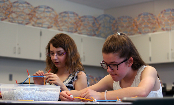 Two students build modules. In the background, shelves are filled with modules completed by earlier classes.