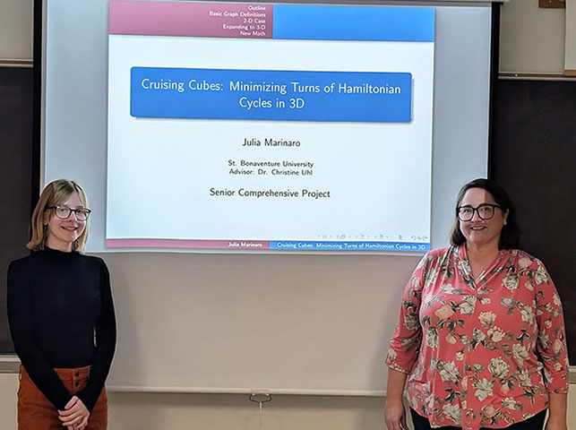 Julia stands with Dr. Uhl in front of a screen showing her title slide.