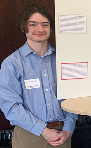 Kyle stands next to a poster for a class project