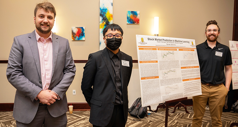 Three students stand next to their project poster.