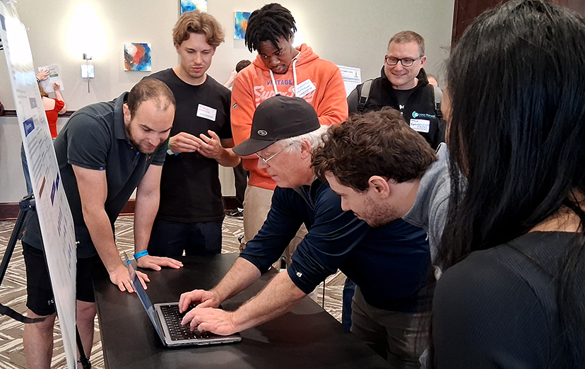 Visitors look at a laptop in front of the project's poster.
