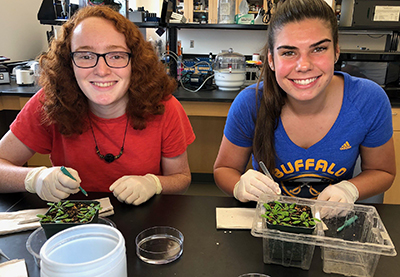 Two female students examining plants in a lab 