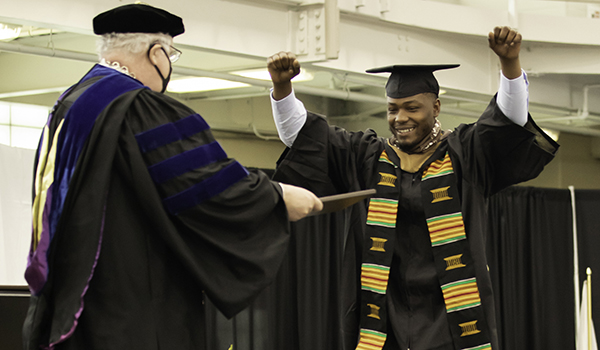 A graduate throws his arms up in the air before receiving his diploma