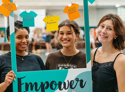 Three students hold a sign reading ‘Empower.’