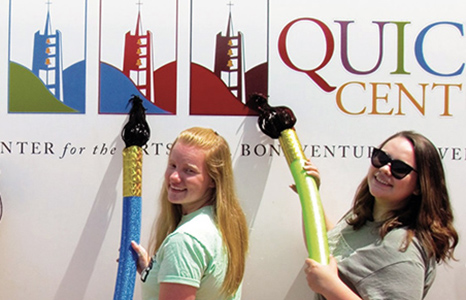 Two Quick Center educators holding giant paint brushes by the traveling Artmobile.