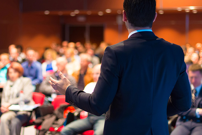 man in blue suit speaking to a crowd