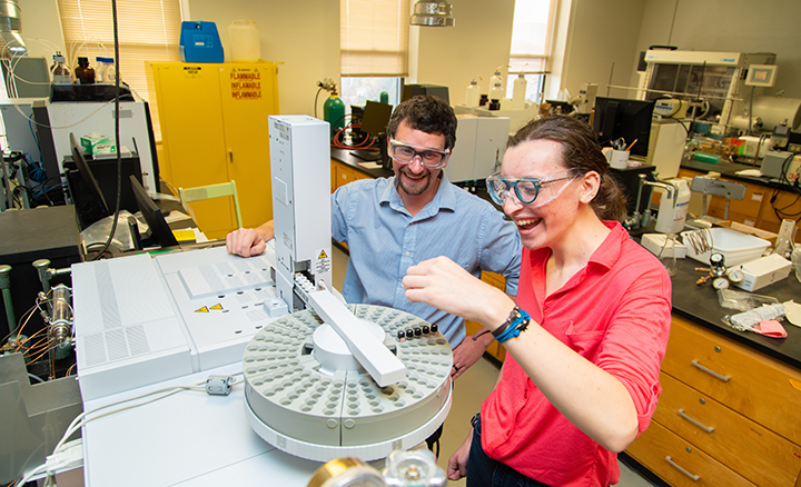 Dr. Scott Simpson looks on as Katharina “Katie” Heitzman, ’22, a dual chemistry/biochemistry major uses a gas chromatograph – mass spectrometer (GC-MS) to identify compounds in the university’s Chemistry Instrumentation Suite.